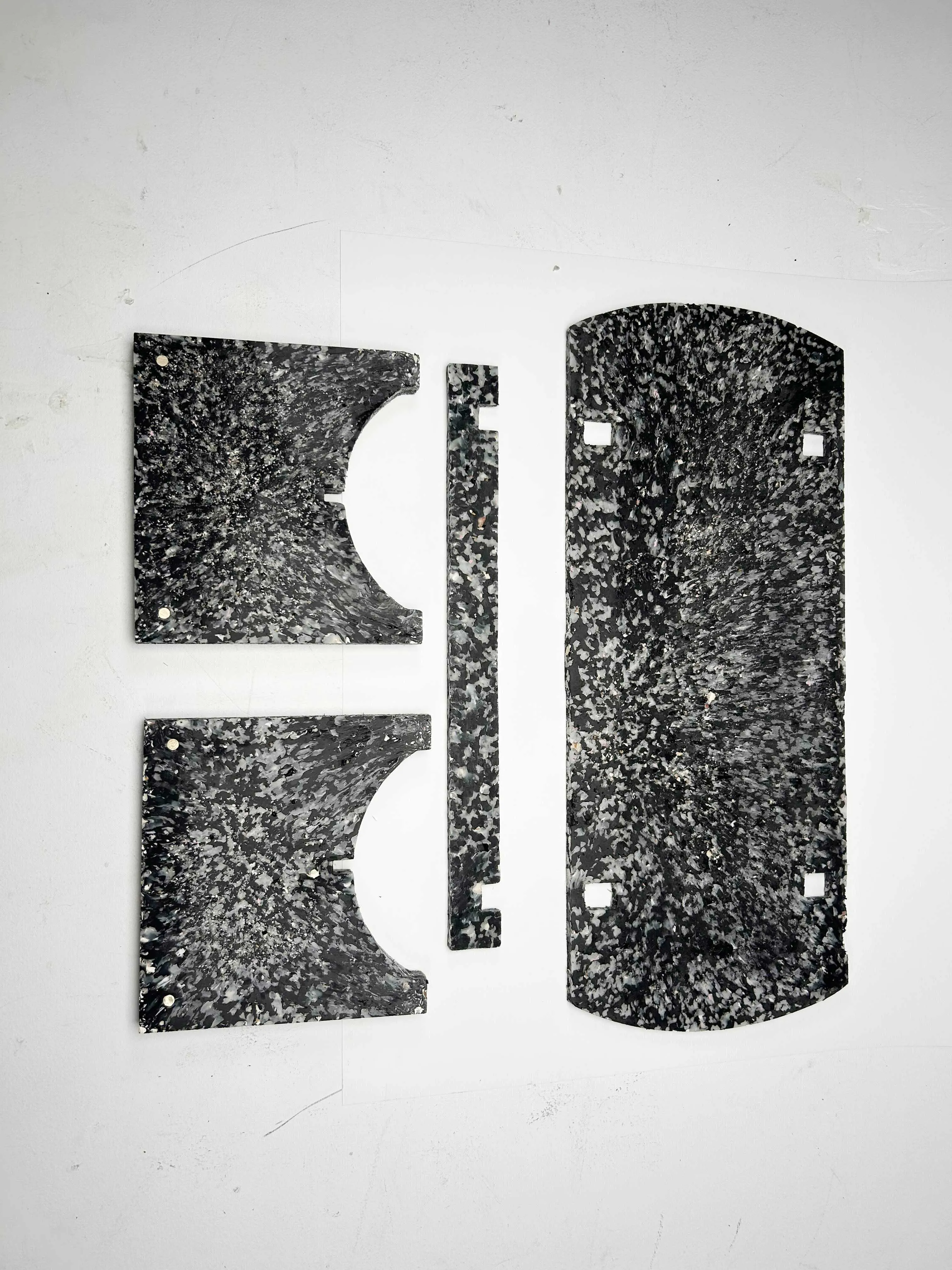 The four flat-pack components of the Shio bench laid out, showing the speckled shell-composite surface.